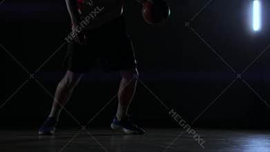 A man with a basketball on a dark basketball court against the backdrop of a basketball ring in the smoke shows