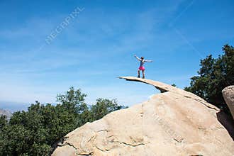 Brave young adult woman hiker stands on top of Potato Chip Rock in San Diego California
