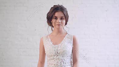Attractive image of dark-haired bride with neat, gentle hairstyle, goes and looks directly at camera, spinning in long