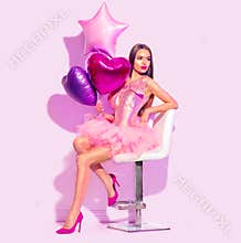 Beauty fashion model party girl with heart shaped air balloons posing, sitting on chair. Birthday party, Valentines Day