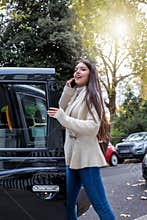 Business woman talking on her mobile phone whilst steps into a black taxi