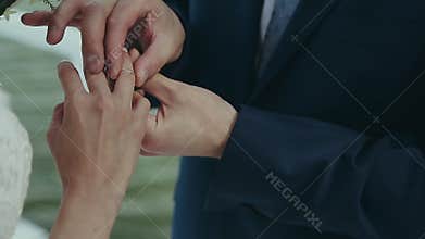 The groom wears a wedding ring on the bride`s finger. Wedding ceremony near the water. Marriage hands with rings close