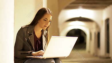 Serious woman typing on a laptop in the night