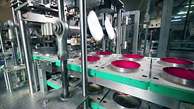 Factory machines placing caps on plastic container on a conveyor.
