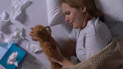 Crying woman hugging teddy bear, used napkins on bed, loneliness after break up