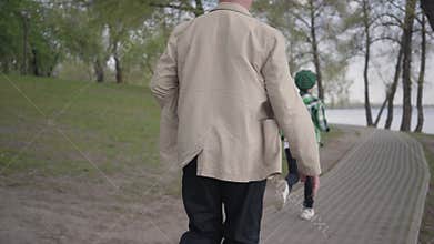 Little boy running away from his grandfather in the park. The old man chasing the boy, but he is tired and stopped to