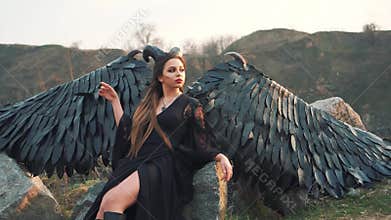 Nightmare queen with long dark flowing hair sits on a big stone, the demon of death rests after a big war, a girl with
