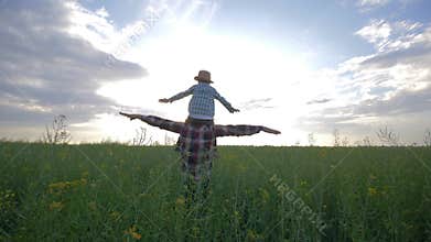 Happy family, son sits on father shoulders and playing with arms raised walking on rapeseed field on background sky in