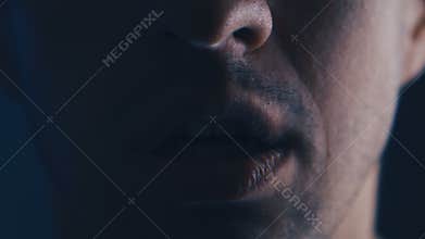 Aggressive man with angry facial expression screaming out loud in dark. Close up of man shouting with mouth wide open.