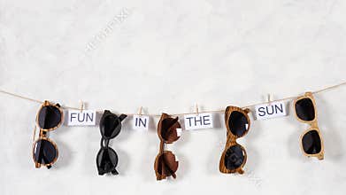 Sunglasses sale concept. Different sunglasses hanging on the rope with phrase fun in the sun on white background. Fashion summer