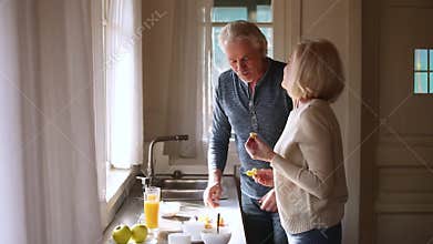 Happy loving senior mature couple having fun preparing healthy breakfast