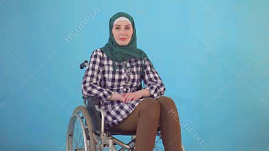 Portrait of a young Muslim woman disabled in a wheelchair on a blue background