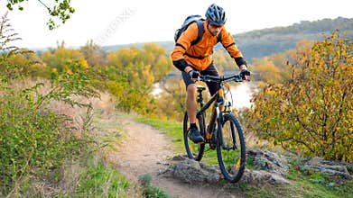Cyclist in Orange Riding the Mountain Bike on the Autumn Rocky Trail. Extreme Sport and Enduro Biking Concept.