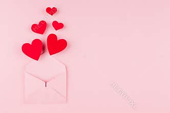 Opened paper envelope with fly out red hearts on soft pink color background. Copy space. Valentine day concept for design.