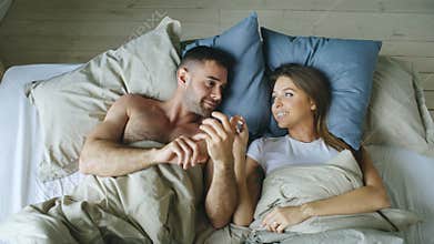 Top view of young couple lying in bed and talking each other smiling