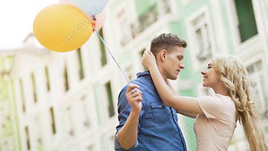 Blonde girl embracing beloved young man, couple dating, holding balloons