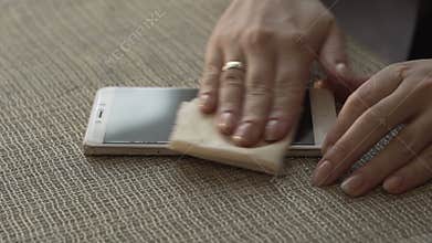 Female hands wiping surface screen mobile phone with cloth close up