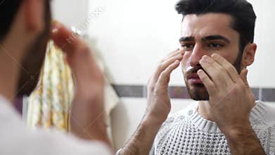 Handsome young man applying moisturizing cream on face