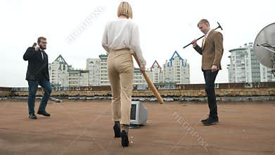 Two men and a girl in suits go to the monitor to break it. A hammer, a bat, violence, hatred, anarchy, destruction, roof