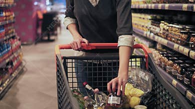 Footage of female costumer picking out products in a grocery store and putting them to shopping push cart while walking