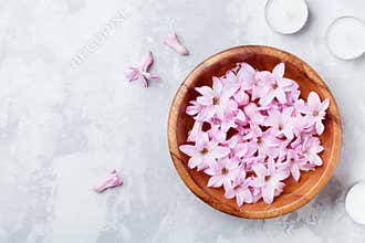 Beauty, spa and wellness composition of perfumed pink flowers water in wooden bowl and candles on stone table. Aromatherapy.
