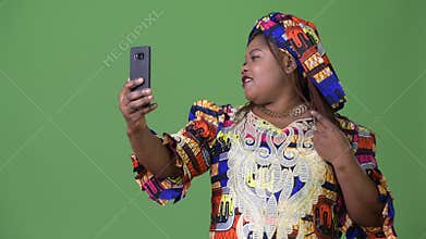 Overweight beautiful African woman wearing traditional clothing against green background