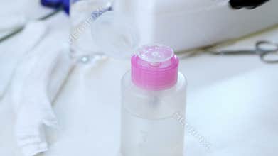 Close-up, the hands of the beautician in black rubber gloves hold the cotton pad and moisten it in a special transparent