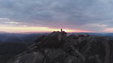 Aerial view of the lonely man standing on top of a cliff and enjoying the sunset.