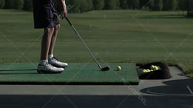 Young golfer practices his golf swing on driving range, view from side