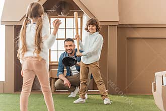 father teaching his kids how to play baseball in front of