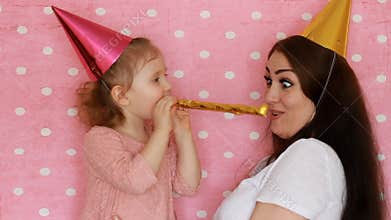 Happy family - Mother and daughter blowing party horns, smiles, hugs, laugh and celebrate birthday. A woman and her