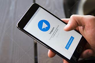 Novosibirsk, Russia - April 30, 2018 - Male hand holding smartphone with the start window of the Telegram application. Wooden back