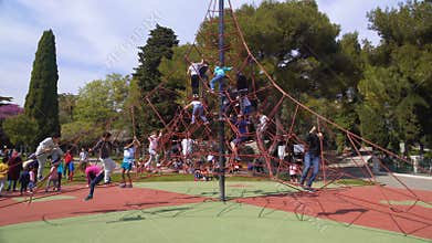 Lots of happy kids climbing on cable spider web at children amusement park
