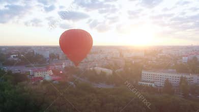 Hot air balloon floating over city at dawn, sun rising on horizon, aspirations