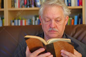 Senior man reads in front of bookcase