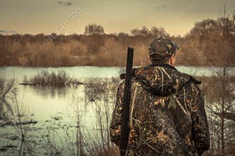 Hunter man shotgun camouflage exploring flood river hunting season rear view sunset
