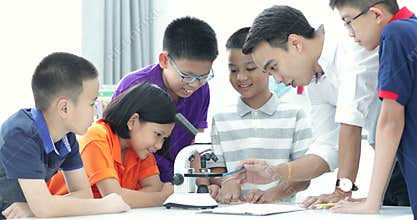 Asian teacher expanding to student in biology class with microscope .
