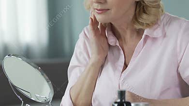 Beautiful middle-aged woman looking in the mirror and touching her skin, care