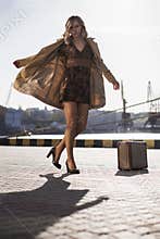 Attractive Young Blonde Woman in Trench with Vintage Suitcase on the Jacht Pier