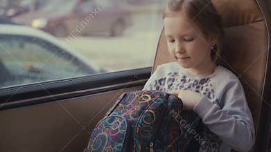 Young, beautiful girl passenger with school bag in the moving school bus using social network on her smartphone and