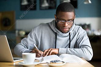 Focused millennial african student making notes while studying i