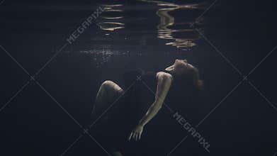 Young woman in black dress swimming underwater in pool while video shooting