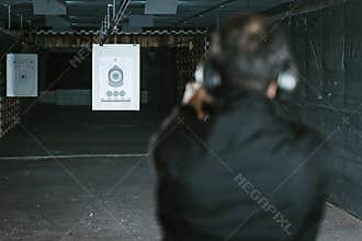 rear view of man aiming gun at target in shooting range