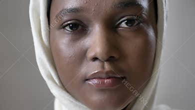 Face ofoung sad african muslim girl in hijab is looks up and watching at camera, religioun concept, grey background