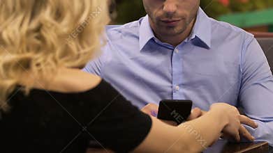 Young man using mobile phone, woman trying to talk to him, indifferent attitude