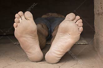 Bare feet of impoverished man resting in hut