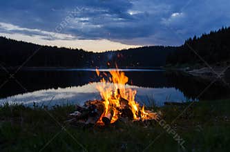 Campfire after sunset in the mountains next to a lake