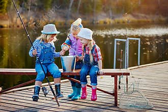 Three little happy girls brag about fish caught on a fishing pole. Fishing from a wooden pontoon