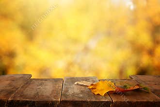 image of front rustic wood table with dry gold leaves and fall bokeh background.