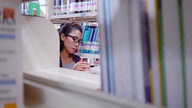 Female student reads book in library aisle